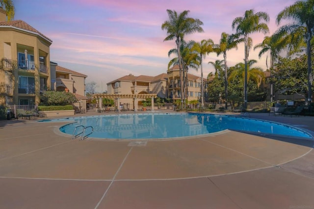 pool at dusk with a pergola and a patio area