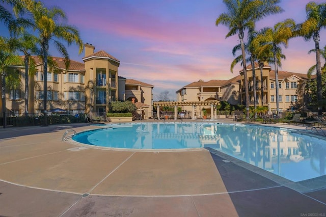 pool at dusk featuring a pergola and a patio