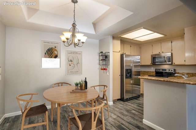 dining area with dark wood-type flooring, an inviting chandelier, a raised ceiling, and sink