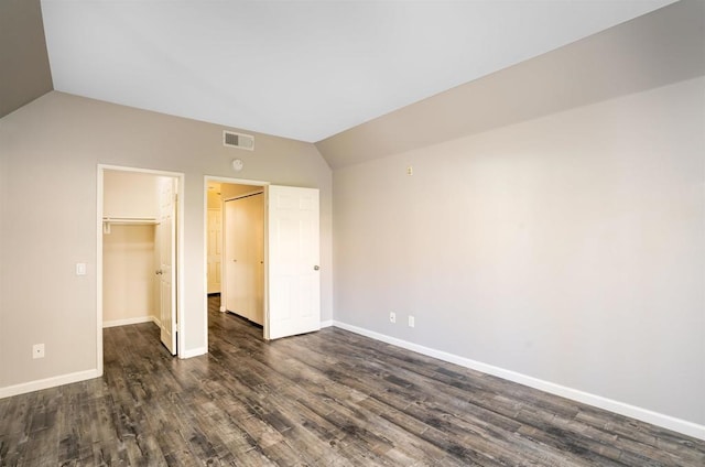 unfurnished bedroom with a closet, a spacious closet, dark hardwood / wood-style flooring, and vaulted ceiling