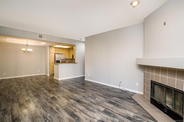 unfurnished living room featuring dark wood-type flooring, a tile fireplace, and a chandelier