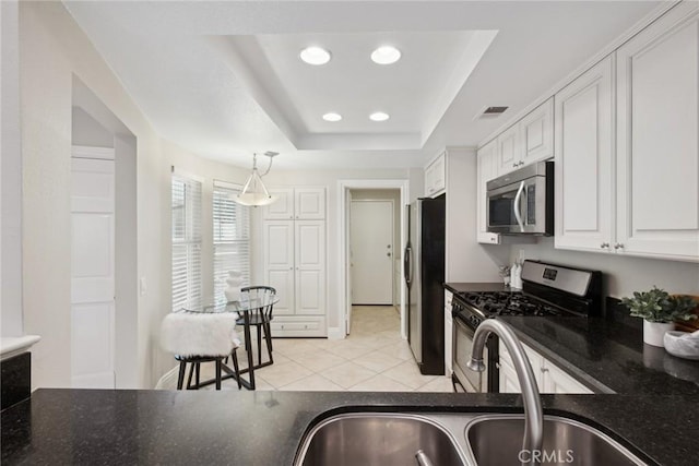 kitchen with pendant lighting, white cabinets, a tray ceiling, stainless steel appliances, and light tile patterned floors