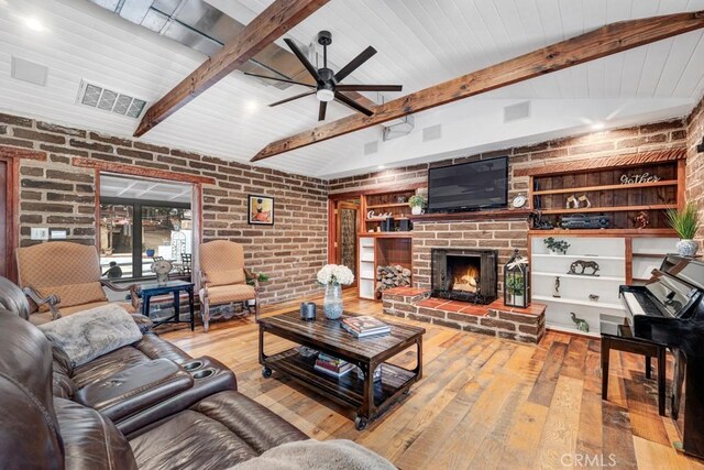 living room with brick wall, vaulted ceiling with beams, light hardwood / wood-style floors, a fireplace, and ceiling fan