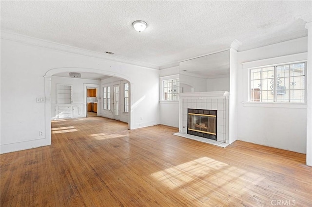 unfurnished living room with a textured ceiling, crown molding, a fireplace, and wood-type flooring