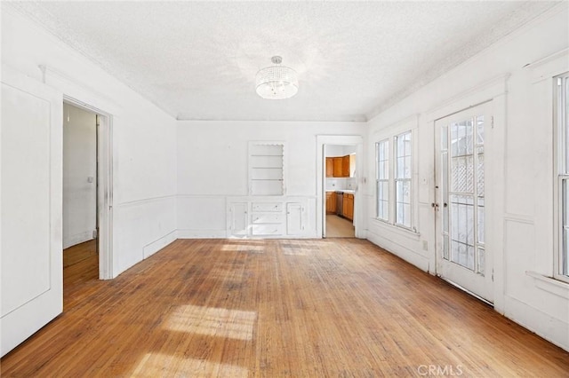 spare room featuring built in shelves, a textured ceiling, and light wood-type flooring