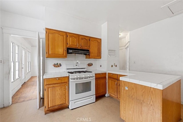 kitchen featuring tile counters, white gas range, kitchen peninsula, and backsplash