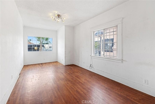 unfurnished room featuring wood-type flooring, an inviting chandelier, and a textured ceiling