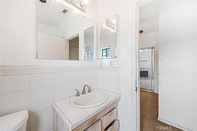 bathroom with toilet, vanity, tile walls, and wood-type flooring