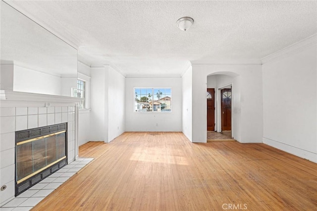 unfurnished living room featuring light wood-type flooring, a tile fireplace, ornamental molding, and a textured ceiling