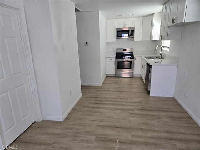 kitchen with sink, white cabinets, appliances with stainless steel finishes, and light hardwood / wood-style flooring