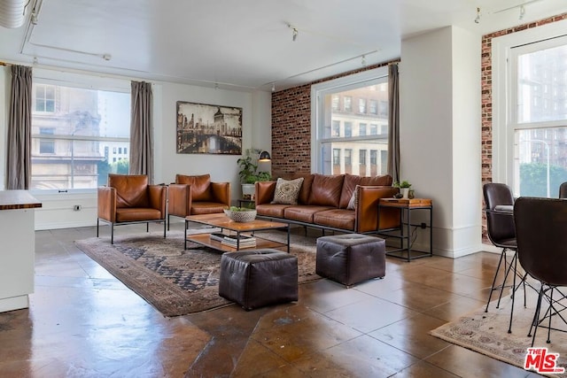 living room featuring track lighting, brick wall, and a wealth of natural light