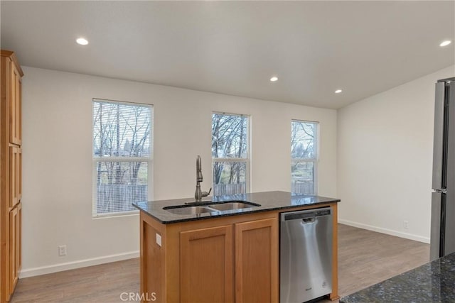 kitchen with appliances with stainless steel finishes, dark stone countertops, sink, a kitchen island with sink, and light wood-type flooring