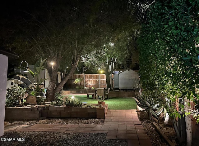 patio at night featuring a lawn and a storage shed