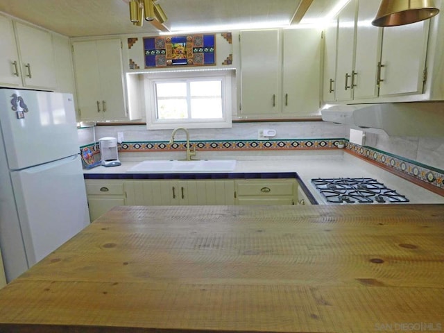 kitchen with decorative backsplash, gas cooktop, sink, white cabinetry, and white refrigerator