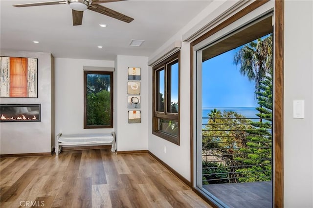 doorway featuring a glass covered fireplace, wood finished floors, baseboards, and ceiling fan