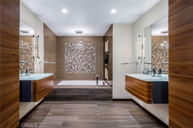 bathroom with a bath, a sink, a chandelier, and two vanities