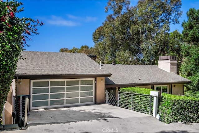 view of front of home with stucco siding, an attached garage, a shingled roof, and driveway