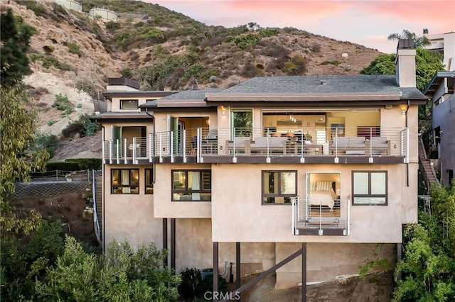 back of house at dusk featuring stucco siding, a mountain view, and a chimney