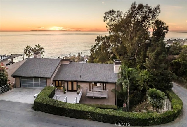 view of front of property with a garage, a water view, driveway, and a chimney