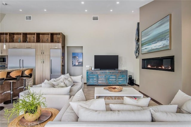 living room with recessed lighting, visible vents, light wood-style floors, and a glass covered fireplace