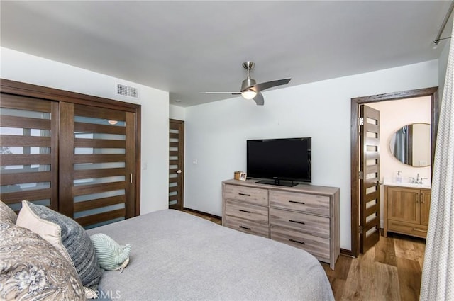 bedroom featuring wood finished floors, visible vents, ceiling fan, a sink, and connected bathroom