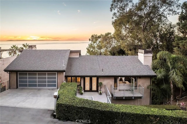 view of front of home featuring driveway, a shingled roof, a chimney, stucco siding, and a garage