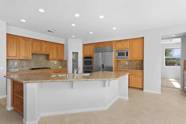 kitchen with light stone counters, a center island with sink, a breakfast bar area, and built in appliances