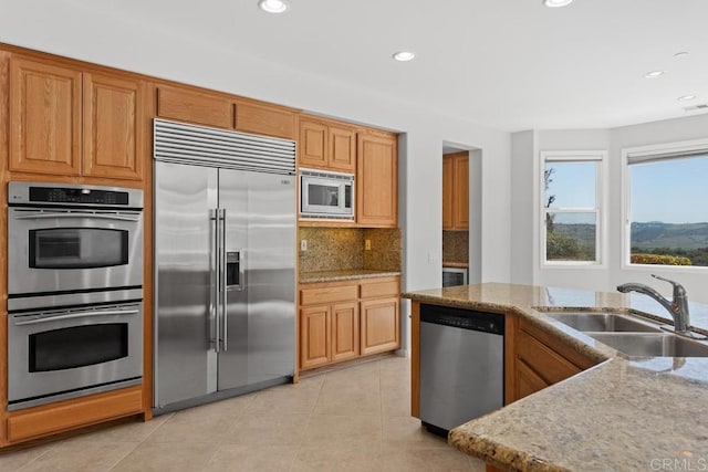 kitchen with decorative backsplash, sink, built in appliances, light tile patterned flooring, and light stone countertops