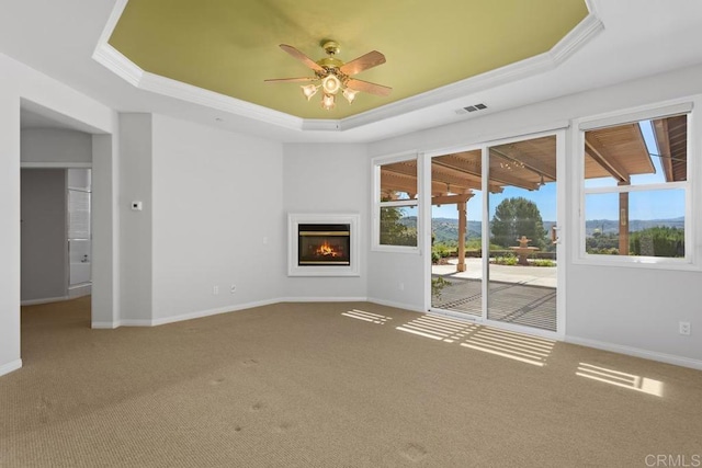 unfurnished living room featuring a raised ceiling, ceiling fan, carpet, and ornamental molding