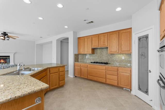 kitchen with ceiling fan, decorative backsplash, gas cooktop, sink, and light stone counters