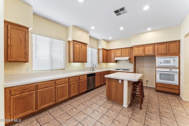 kitchen with a kitchen bar, a center island, white appliances, light tile patterned flooring, and sink