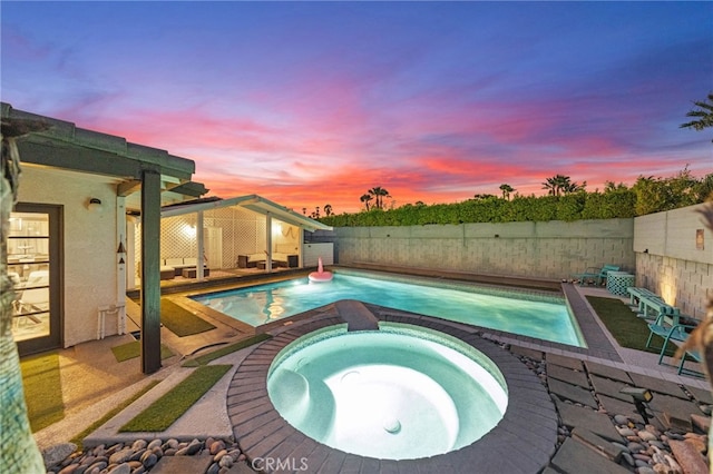 pool at dusk featuring a patio area and an in ground hot tub