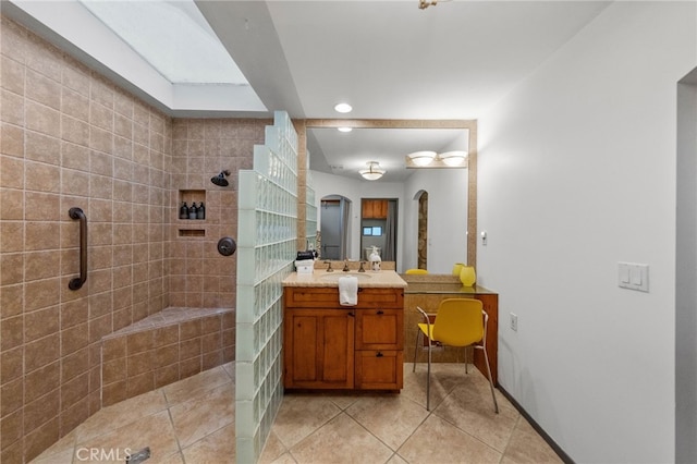 bathroom with tile patterned flooring, a tile shower, and vanity