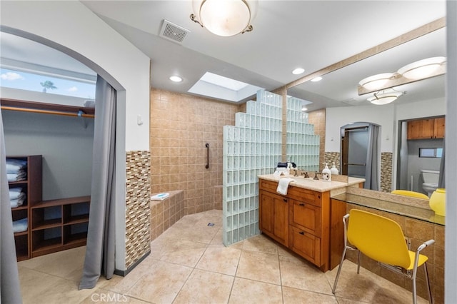 bathroom featuring tile patterned flooring, vanity, tile walls, toilet, and walk in shower