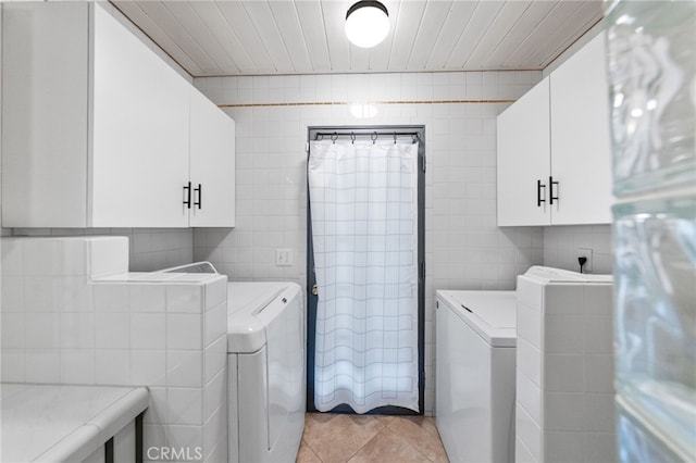 laundry room featuring cabinets, tile walls, light tile patterned floors, and washing machine and dryer