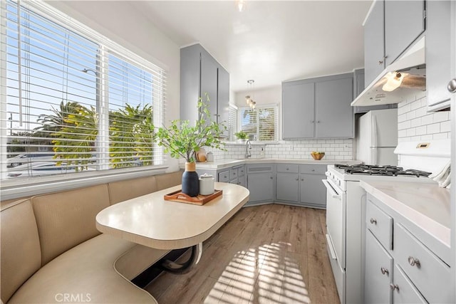 kitchen featuring tasteful backsplash, gray cabinetry, hanging light fixtures, white appliances, and light wood-type flooring