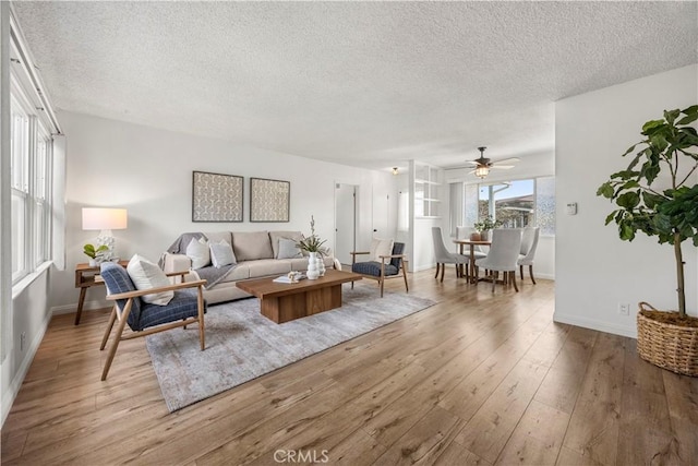 living room featuring ceiling fan, a textured ceiling, and light wood-type flooring