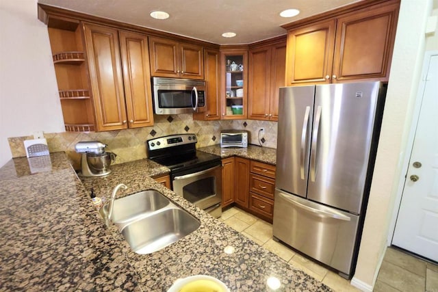 kitchen with appliances with stainless steel finishes, decorative backsplash, light tile patterned flooring, dark stone countertops, and sink