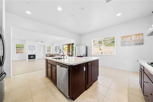 kitchen with ceiling fan, a center island with sink, stainless steel dishwasher, sink, and dark brown cabinetry