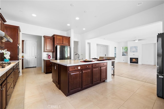 kitchen with ceiling fan, exhaust hood, appliances with stainless steel finishes, and an island with sink