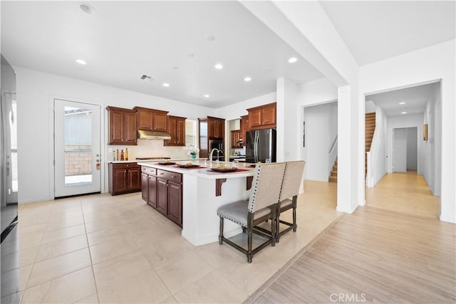 kitchen with a breakfast bar, stainless steel fridge, gas cooktop, and a center island with sink