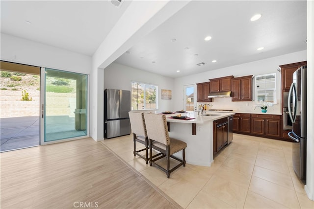 kitchen featuring an island with sink, appliances with stainless steel finishes, backsplash, light hardwood / wood-style flooring, and a breakfast bar