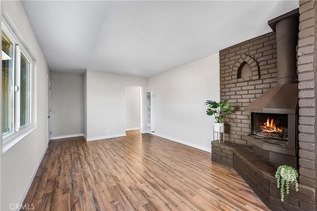 unfurnished living room with wood-type flooring and a brick fireplace