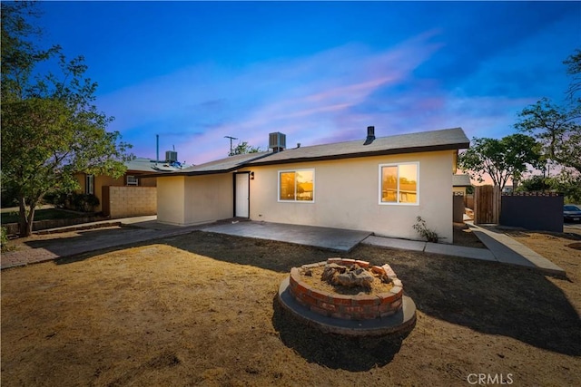 back house at dusk featuring a patio area, a fire pit, and central AC