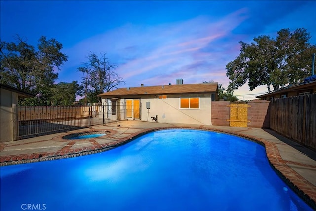 pool at dusk with an in ground hot tub and a patio