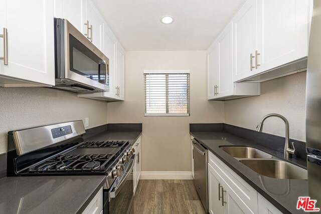 kitchen with appliances with stainless steel finishes, dark hardwood / wood-style flooring, white cabinets, and sink