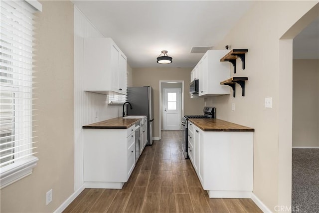 kitchen featuring butcher block countertops, appliances with stainless steel finishes, sink, and white cabinetry