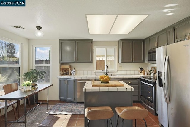 kitchen with tile countertops, stainless steel appliances, a center island, dark tile patterned flooring, and sink