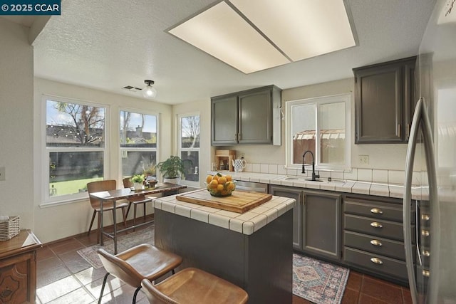 kitchen with tile counters, stainless steel appliances, dark tile patterned flooring, a kitchen island, and sink