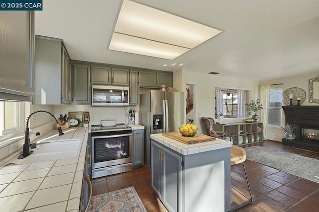 kitchen featuring appliances with stainless steel finishes, a center island, tile counters, a fireplace, and sink